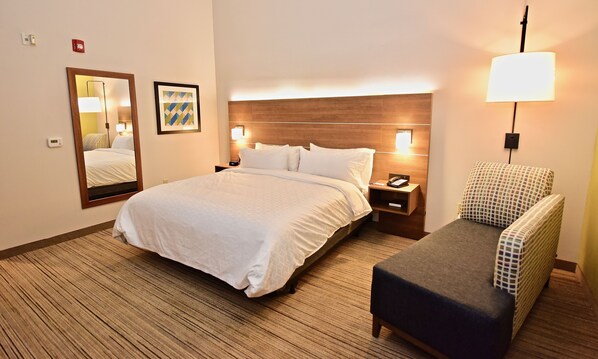 A hotel room with a large bed, a nightstand, a lamp, a chair, and a mirror. - Holiday Inn Express & Suites Perryville by IHG (Perryville)