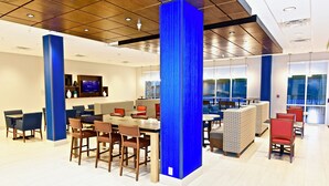 A modern dining area with high tables and chairs, a television screen, and a view of the outdoors through large windows. - Holiday Inn Express & Suites Perryville by IHG (Perryville)