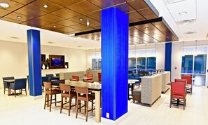A modern dining area with high tables and chairs, a television screen, and a view of the outdoors through large windows. - Holiday Inn Express & Suites Perryville by IHG (Perryville)