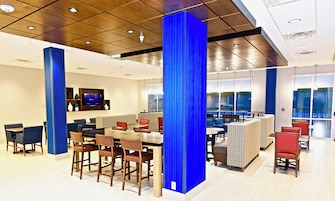 A modern dining area with high tables and chairs, a television screen, and a view of the outdoors through large windows.