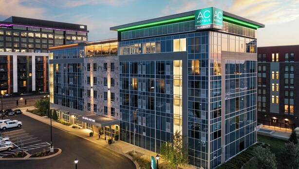 Un hotel moderno con fachada de vidrio, varios pisos y un llamativo letrero AC Hotels Marriott.