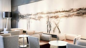 Un vestíbulo moderno con un cuadro abstracto grande, asientos cómodos y una lámpara de pie.