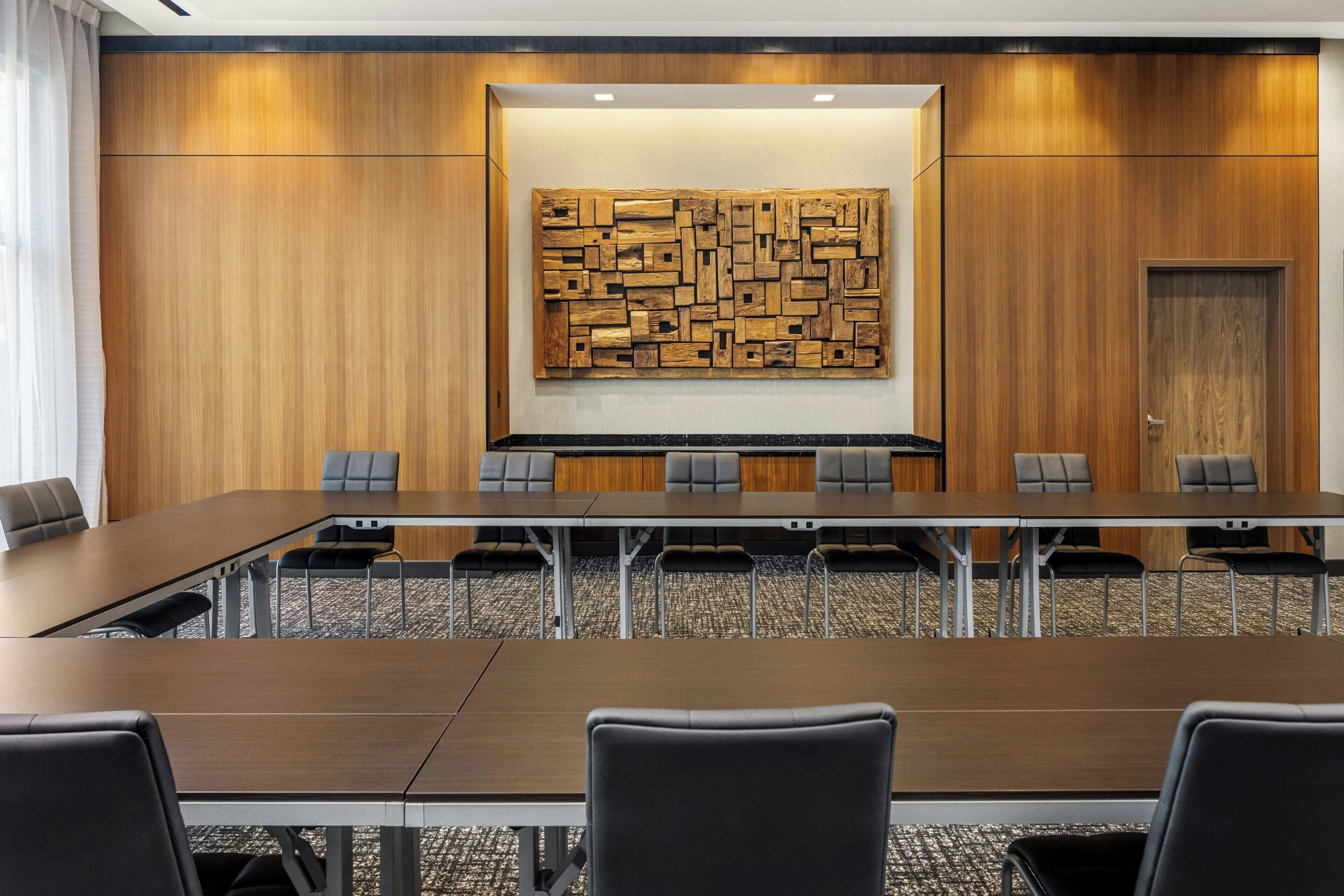 Un salón de conferencias con una larga mesa, varias sillas y un panel de madera decorativo.