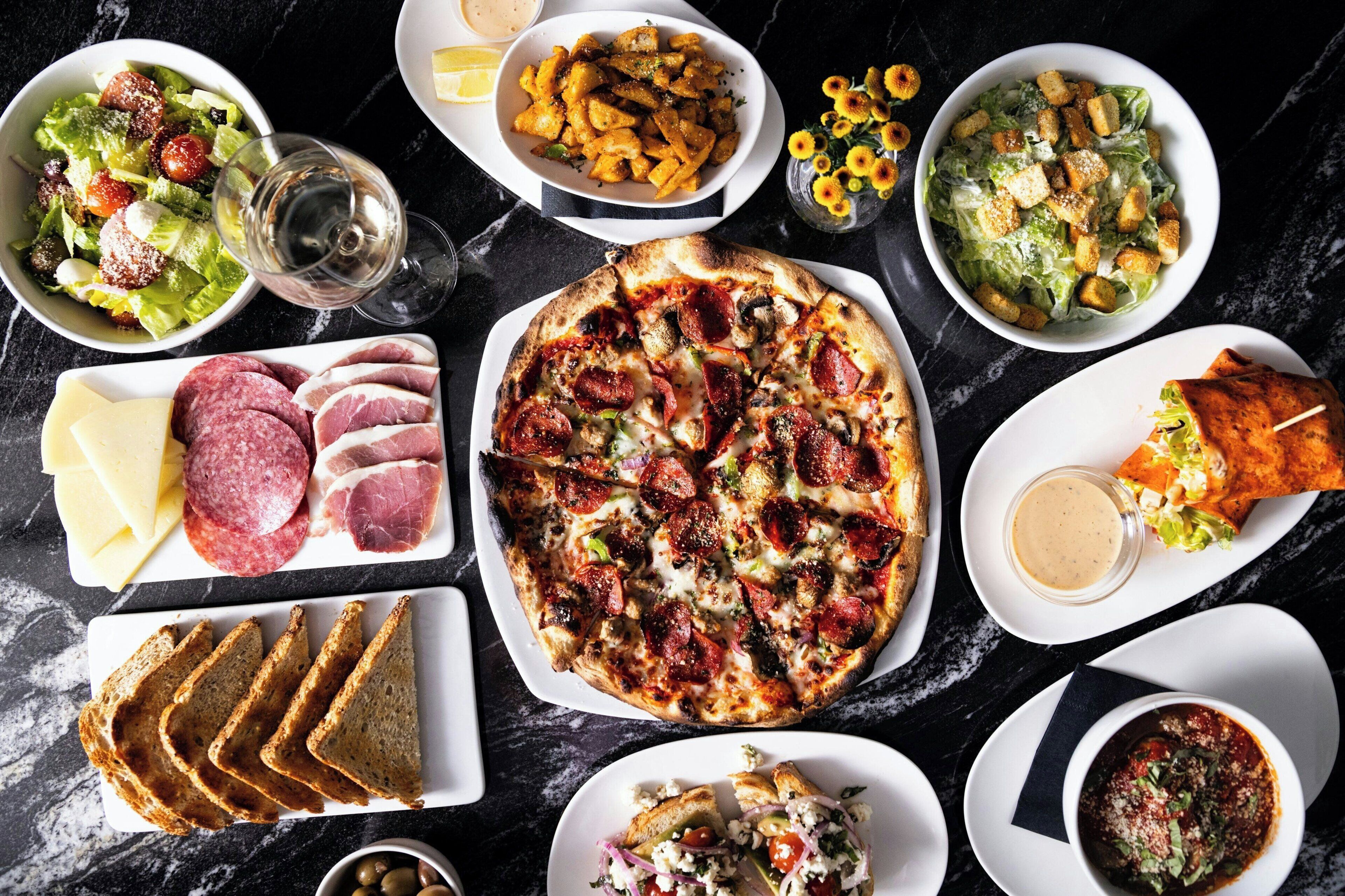 A variety of dishes including pizza, salads, and bread on a marble table.