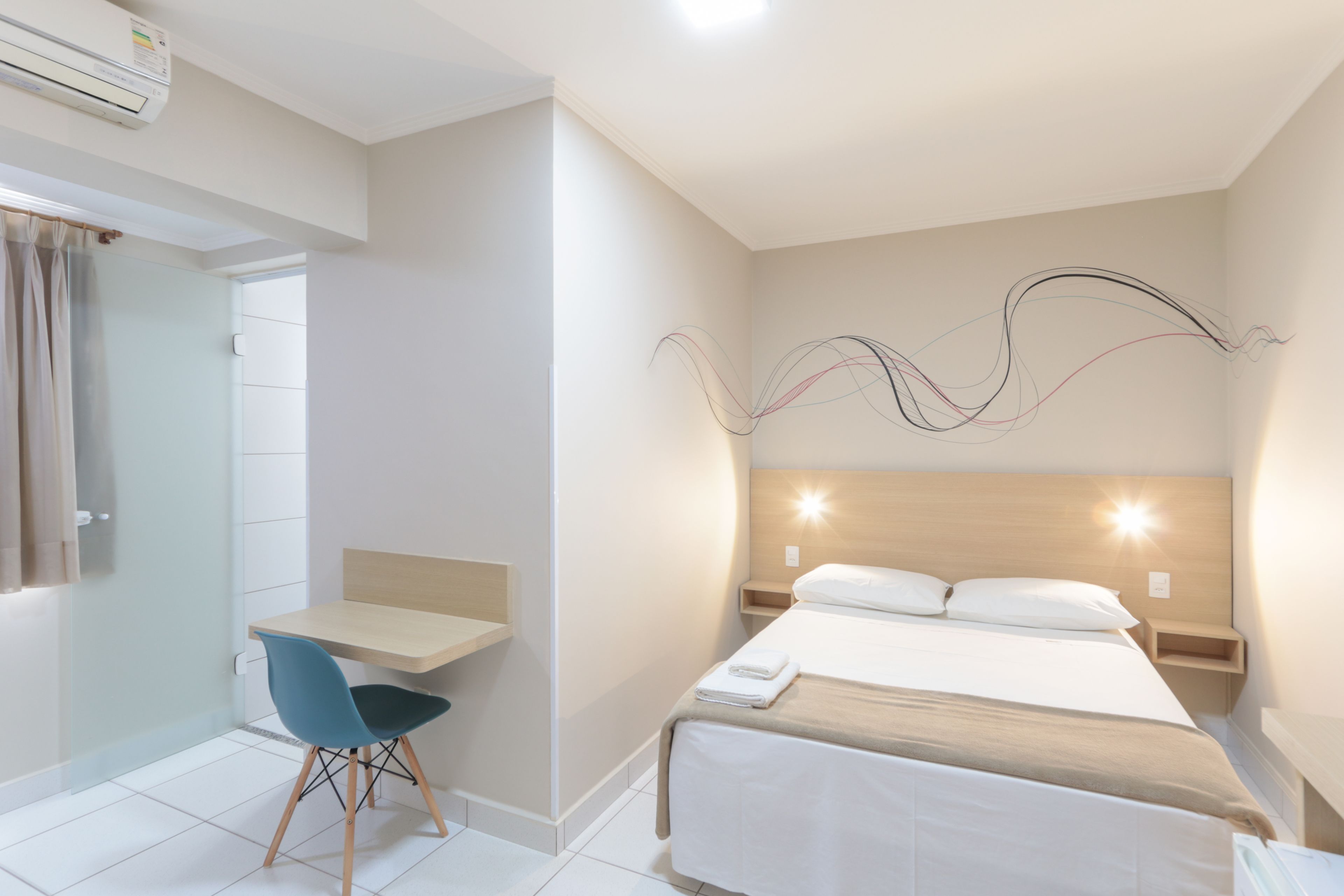 Une chambre d’hôtel comprenant un lit, une table de chevet, une chaise et une œuvre d’art murale.