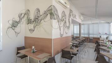 Un moderno comedor con una larga mesa y sillas, una instalación artística en la pared y un amplio ventanal que proporciona luz natural.