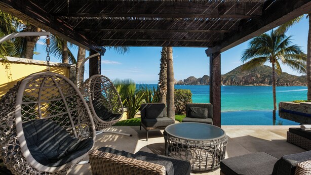 A covered outdoor seating area with wicker furniture, a round table, and a view of the ocean.