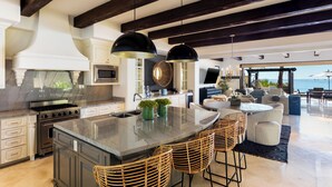 A modern kitchen with a large island, bar stools, and a view of the ocean.
