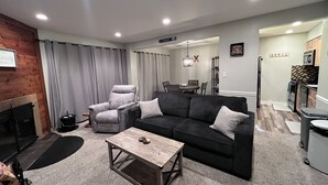 A modern living room with a fireplace, a grey armchair, a black sofa, and a wooden coffee table. - Trail Creek: Ski home to renovated 1st floor, 1br condo. Sleeps 4. (Killington)