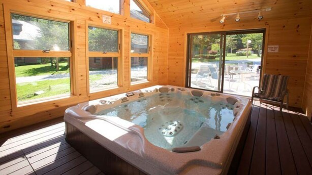 A wooden spa room with a hot tub, large windows, and a view of the outdoors. - Trail Creek: Ski home to renovated 1st floor, 1br condo. Sleeps 4. (Killington)