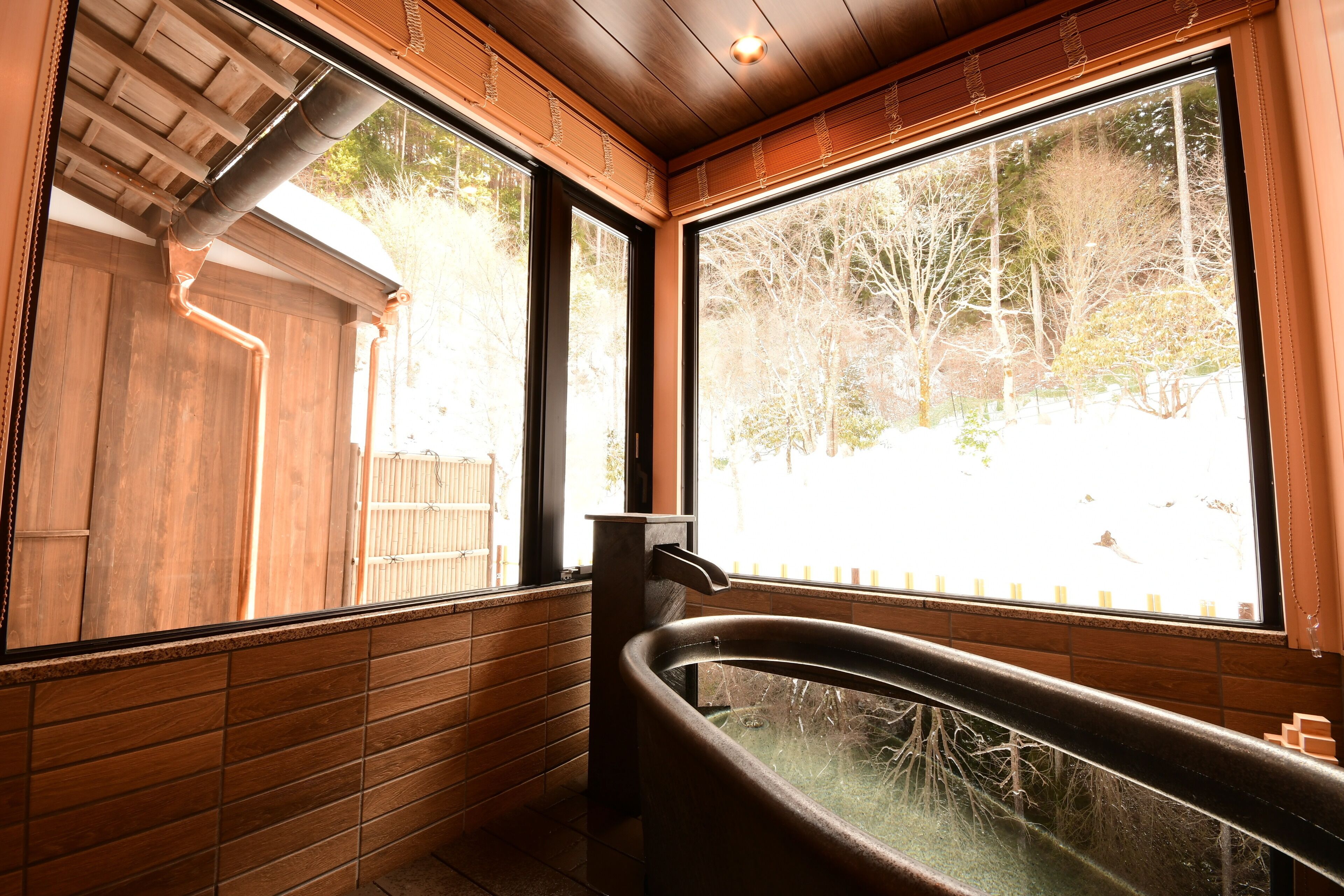 Un baño con bañera, paredes de madera y ventanas amplias que dan a árboles y una valla.