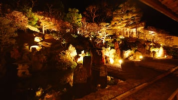 A nighttime view of a traditional Japanese garden with illuminated pathways and stone lanterns.