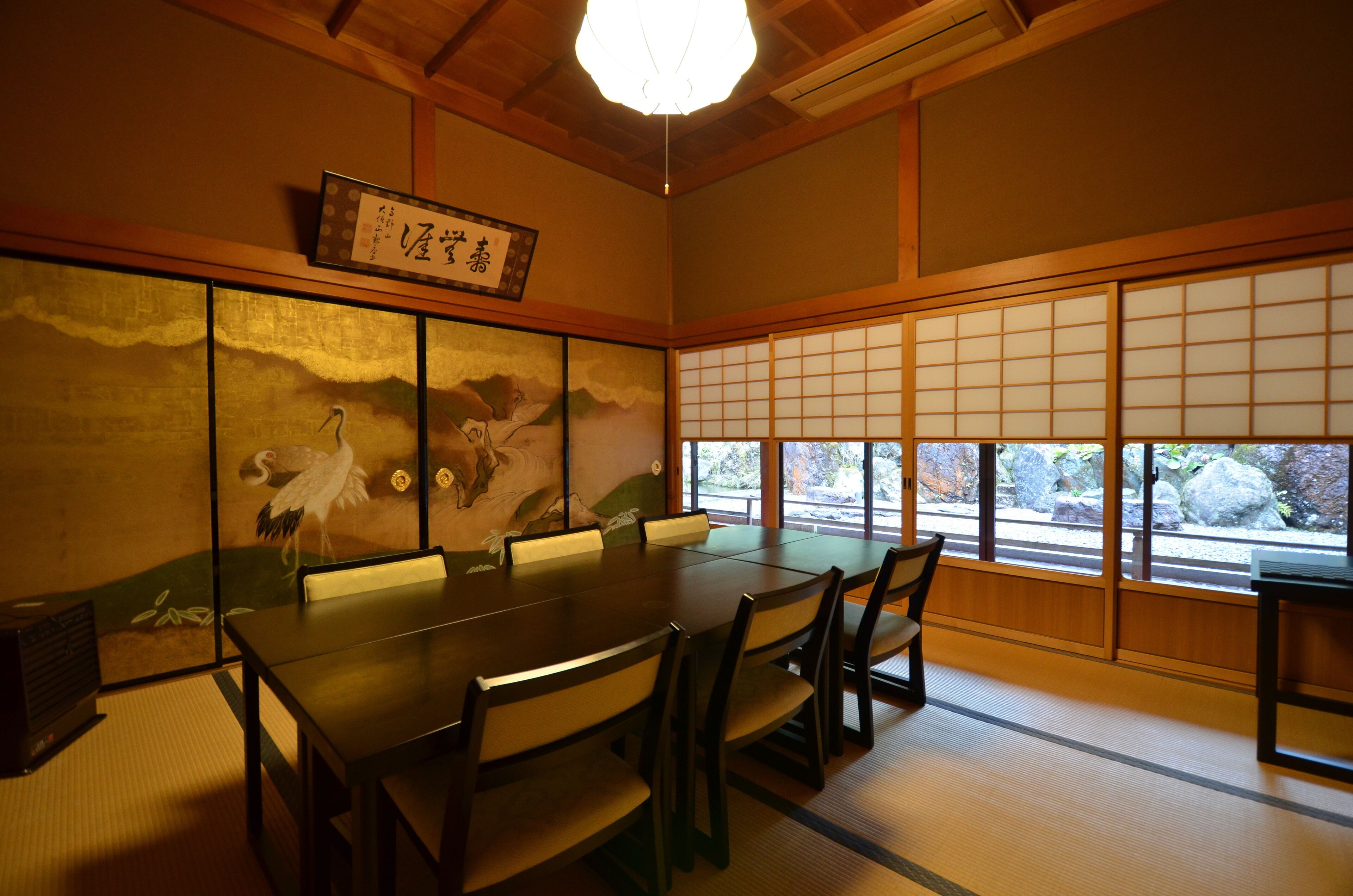 A traditional Japanese room with tatami flooring, a low table with chairs, sliding shoji doors, and a view of the outdoors.