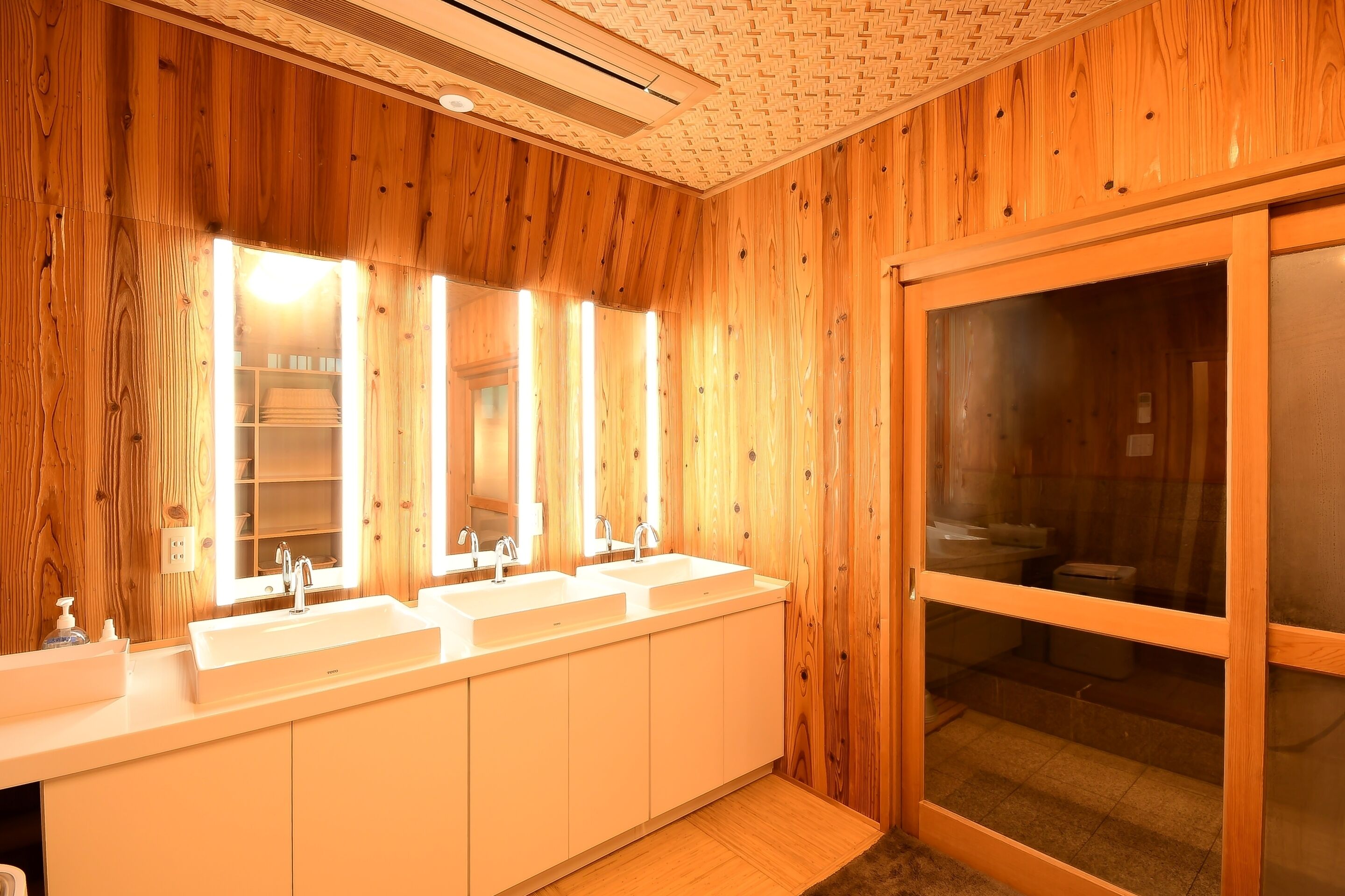 A wooden-paneled bathroom with two sinks, a mirror, and a glass door leading to a shower area.