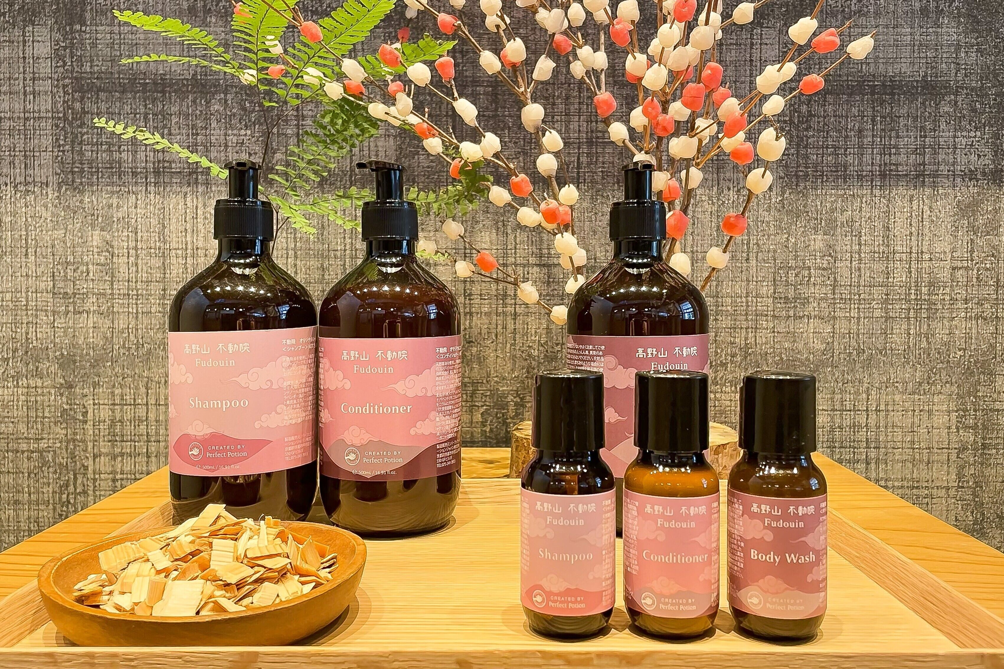 Exhibición de productos Fudouin, incluyendo champú, acondicionador y gel de baño, con un cuenco de flores secas al frente.