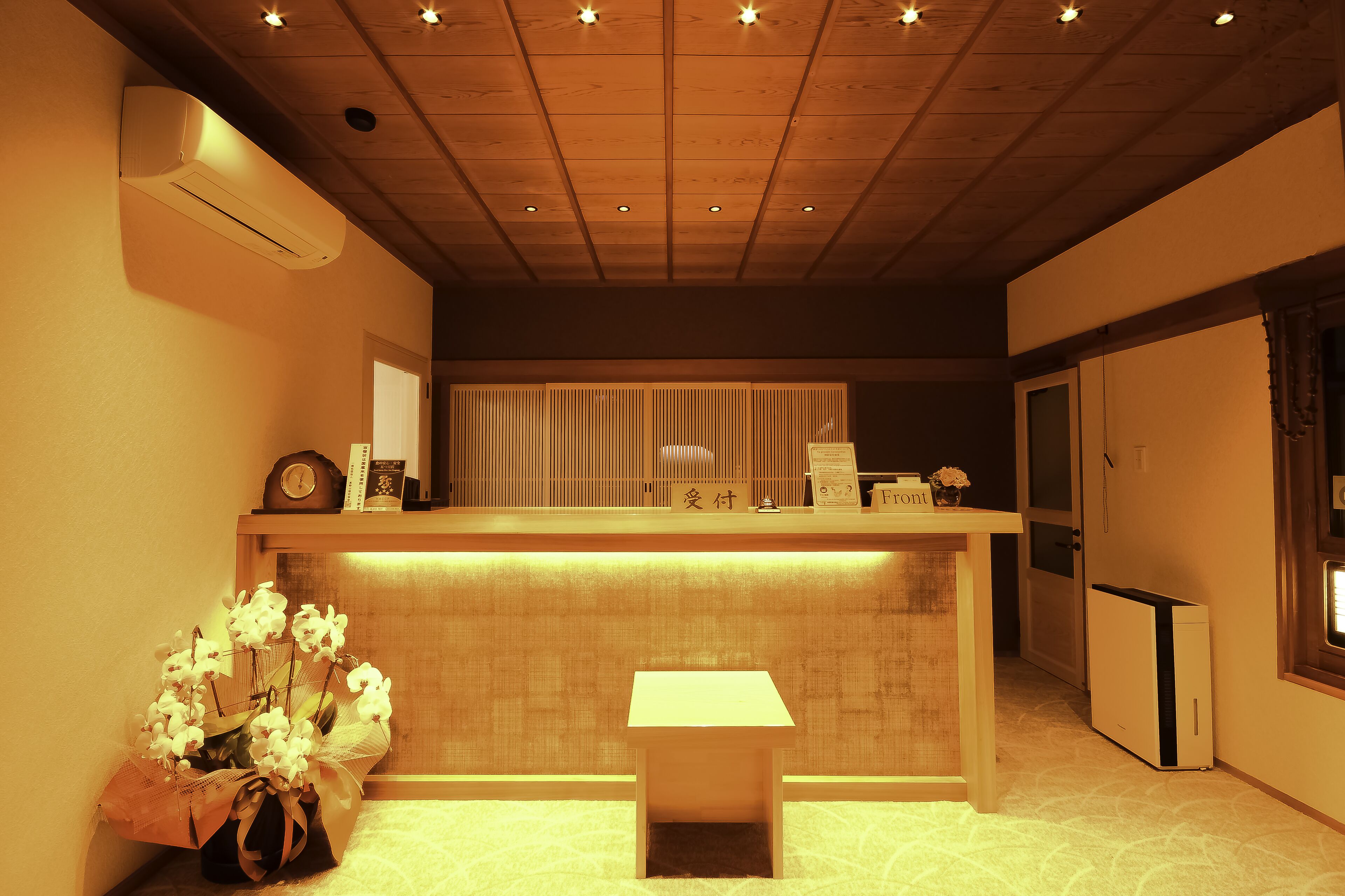 A reception area with a wooden counter, a small table, and a decorative orchid arrangement.