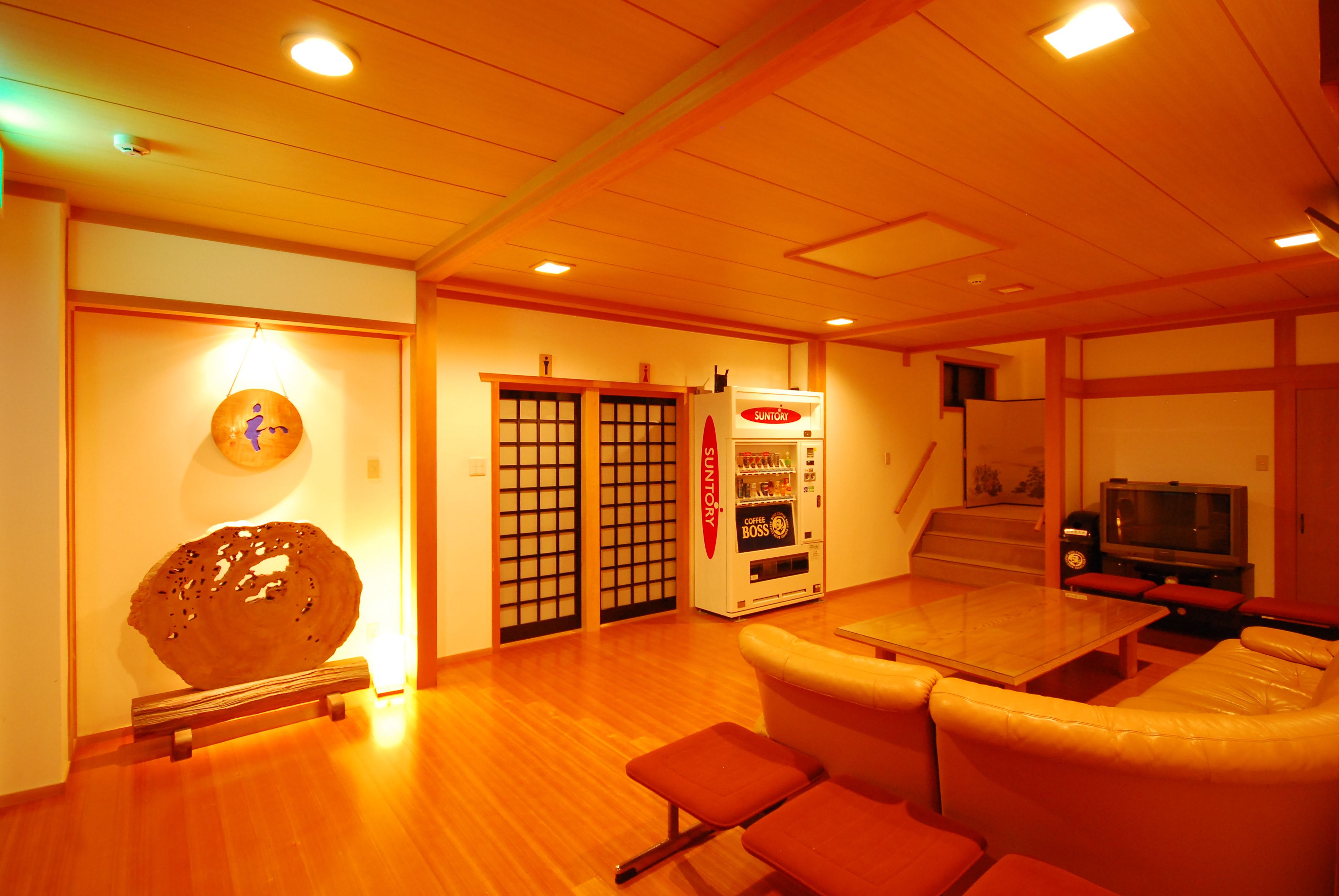 A room with a wooden floor, a glass table, a sofa, a vending machine, and a television.