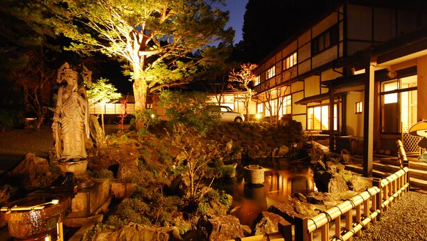A traditional Japanese garden with a stone statue, koi pond, and a building with wooden architecture. - Koyasan Syukubou Fudouin (Koya)
