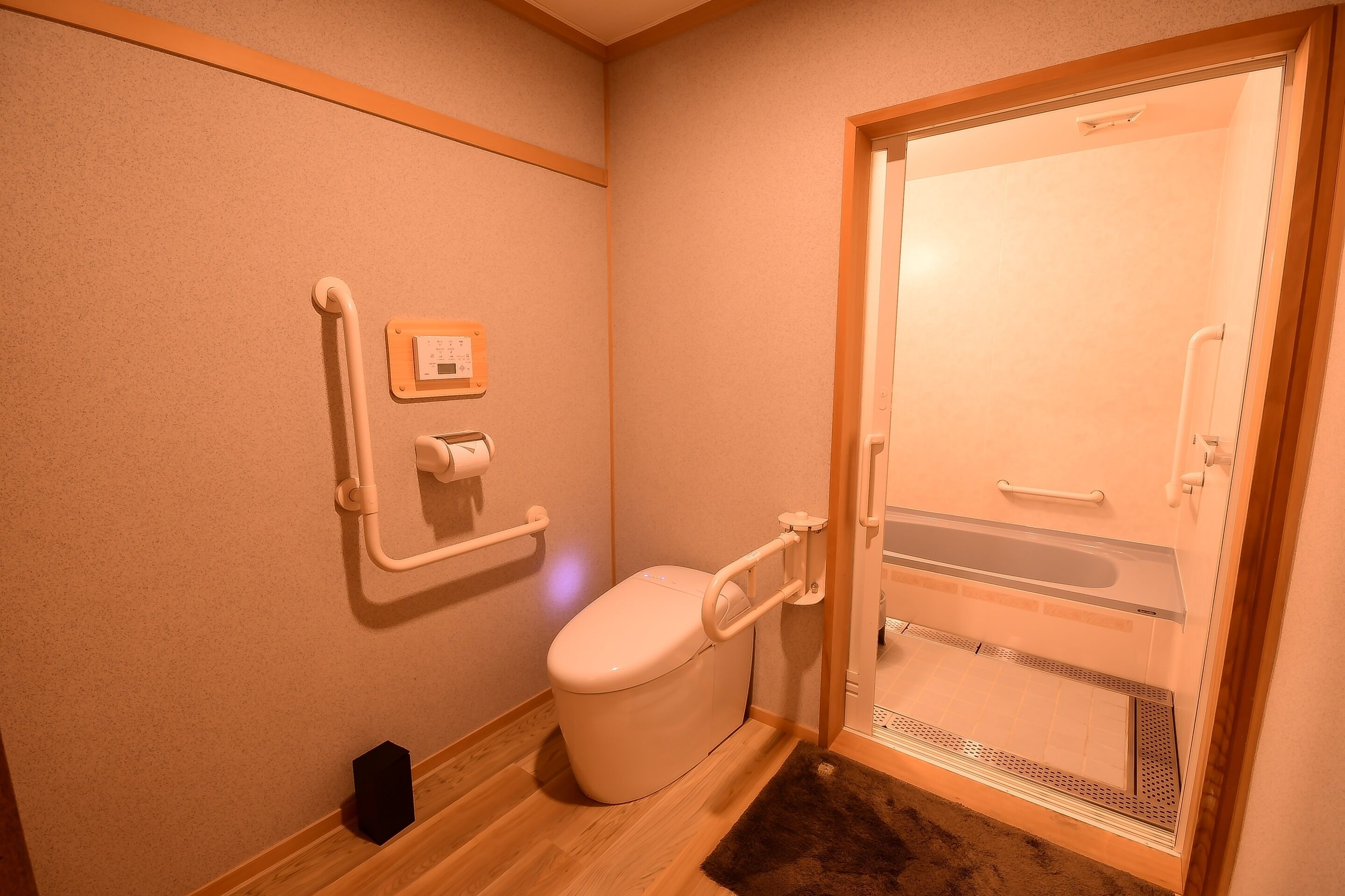 A bathroom with a toilet, grab bars, a hand dryer, and a shower door.