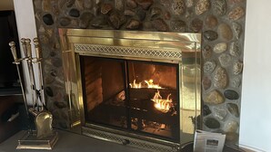 A fireplace with a stone surround and a metal grate, a mantelpiece with a painting, and a rustic chair.
