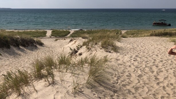 A beach with sand dunes and a boat in the water.