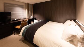 A hotel room with a large bed, a desk with a chair, a television, and a window with curtains.