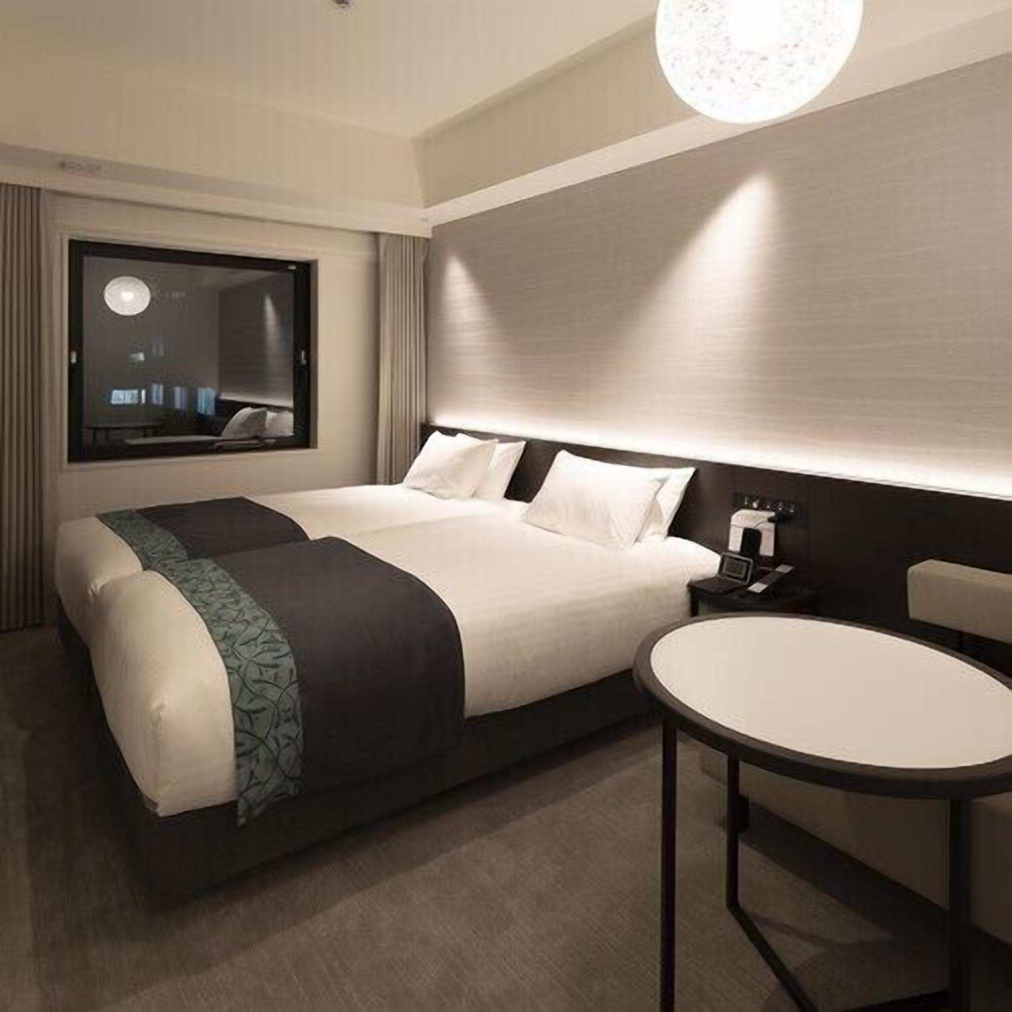 A modern hotel room with a large bed, bedside table, and a round table.