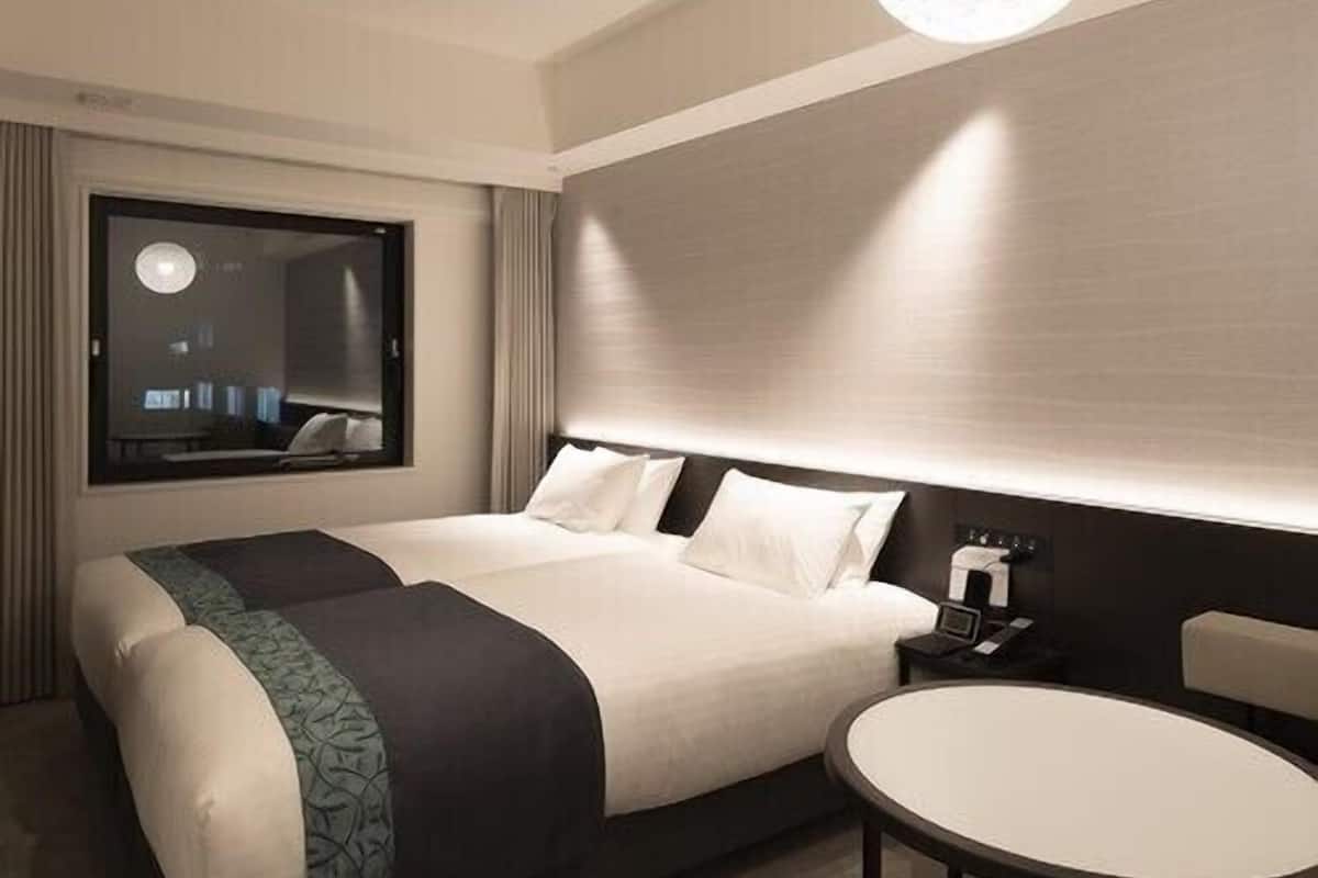 A modern hotel room with a large bed, bedside table, and a round table.