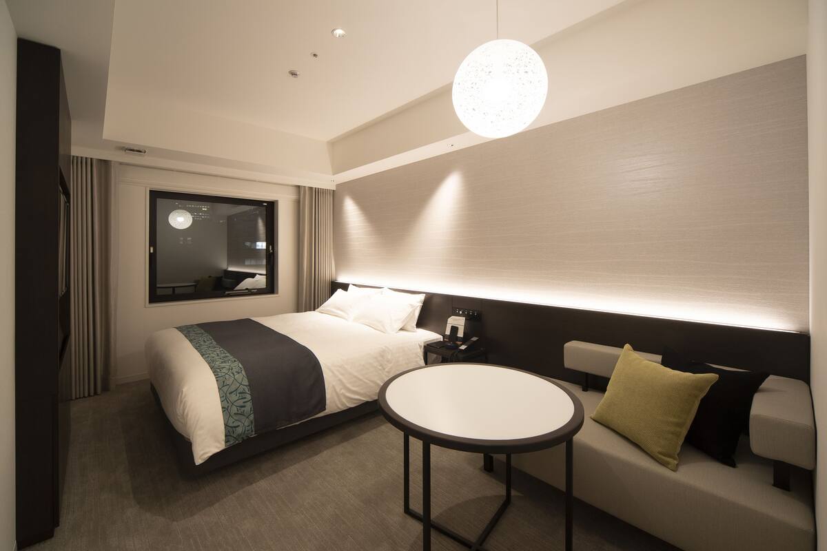 A hotel room with a bed, bedside table, and a round table.