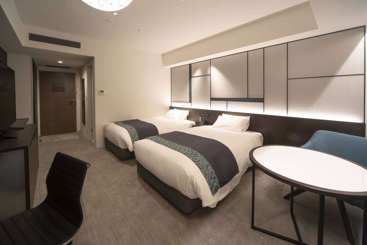 A hotel room with two beds, a desk, a chair, and a round table.