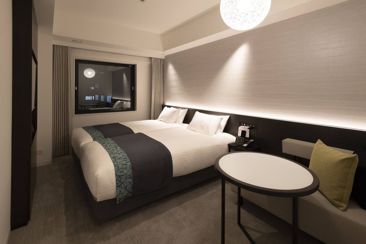 A modern hotel room with a large bed, bedside table, and a round table.