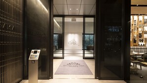 A hotel entrance with a modern design, a reception desk, and a visible elevator. - Hotel Vischio Osaka (Osaka)