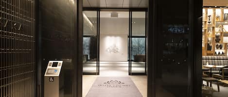 A hotel entrance with a modern design, a reception desk, and a visible elevator.