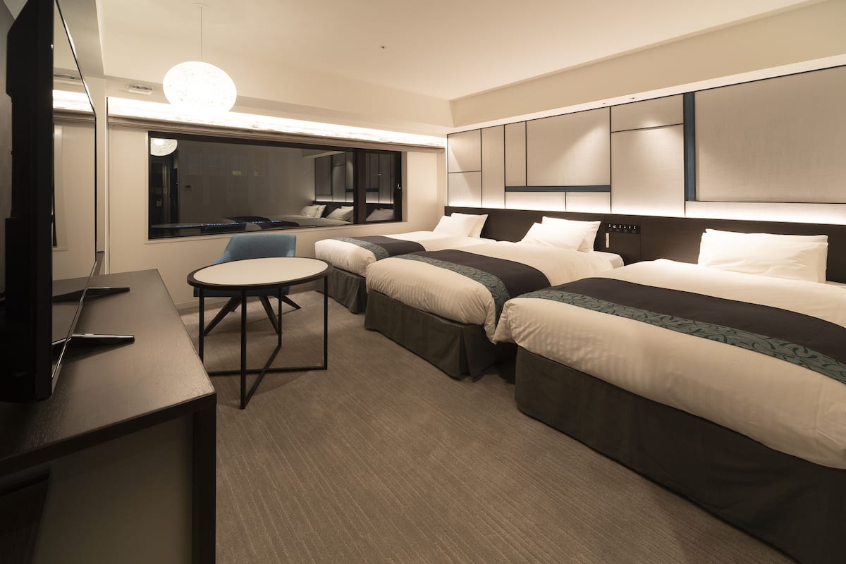 A hotel room with two beds, a desk, a chair, and a TV.