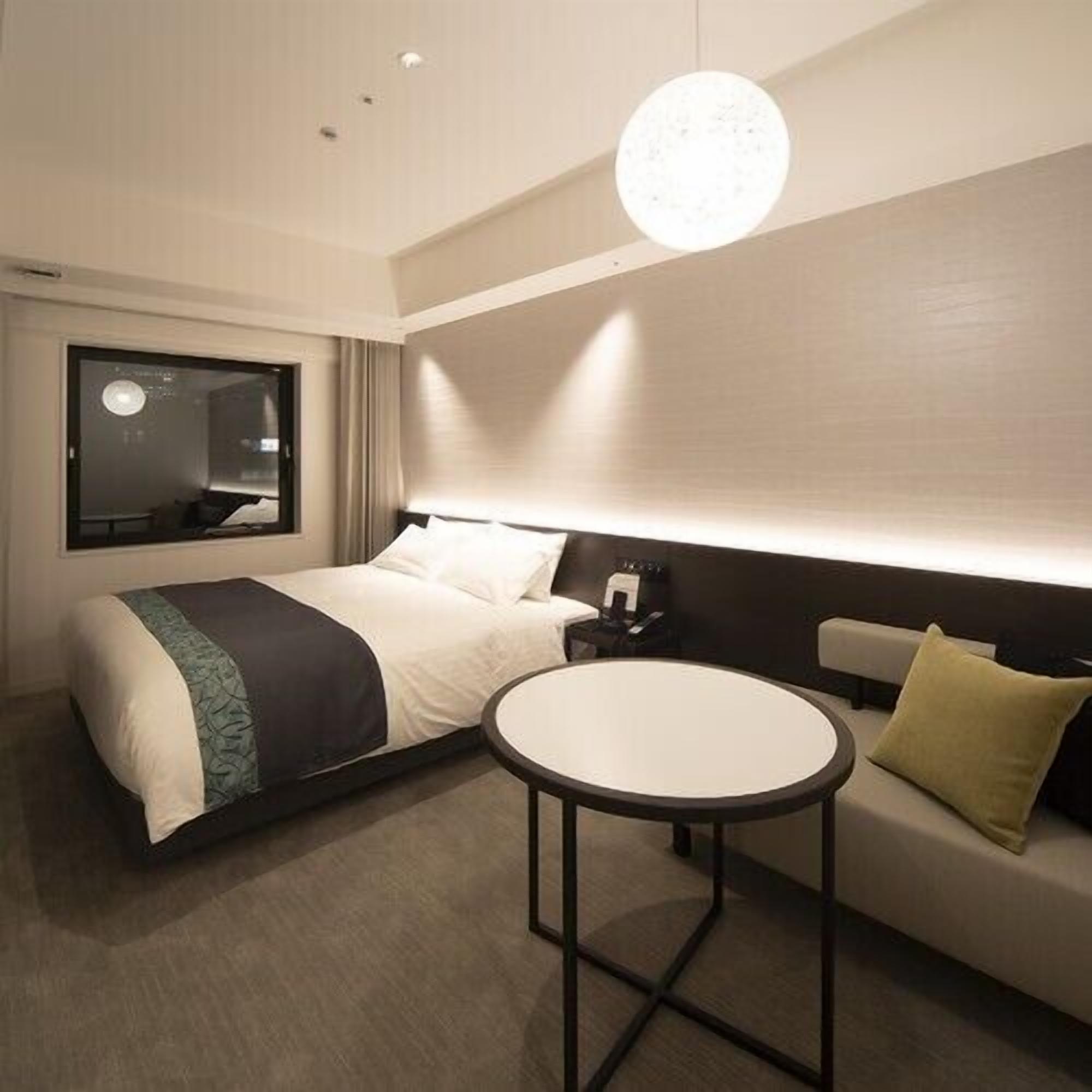 A modern hotel room with a bed, a round table, a sofa, and a large mirror.
