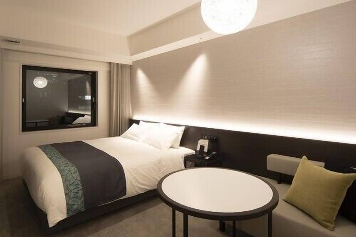 A modern hotel room with a bed, a round table, a sofa, and a large mirror.