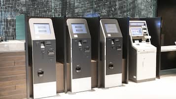 Una hilera de cajeros automáticos con un diseño moderno, que incluyen una pantalla digital y lector de tarjetas, frente a una pared con un patrón decorativo.