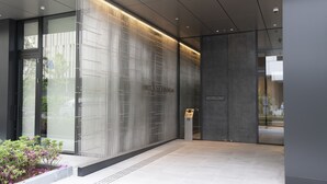 A modern building entrance with a glass door, a vertical metal panel, and a small sign. - Hotel Vischio Osaka (Osaka)