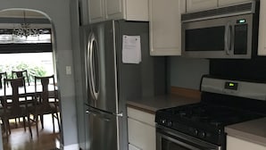 A modern kitchen with stainless steel appliances, white cabinetry, and a wooden dining area.