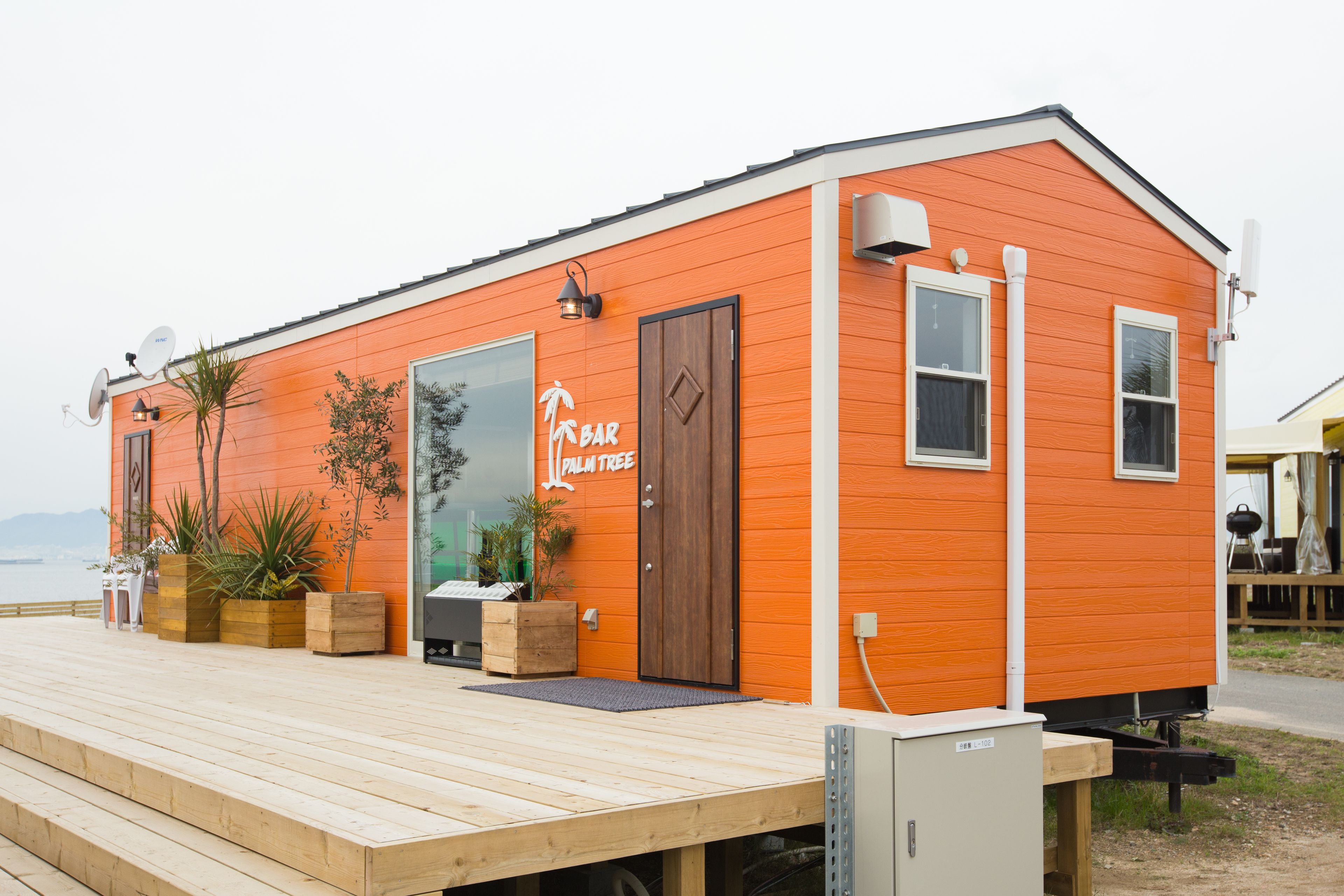 A small, orange building with a wooden deck, a sign reading "Palm Tree Bar," and potted plants.