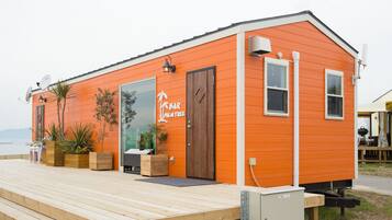 Un pequeño edificio naranja con una terraza de madera, un letrero que dice "Palm Tree Bar" y plantas en macetas.