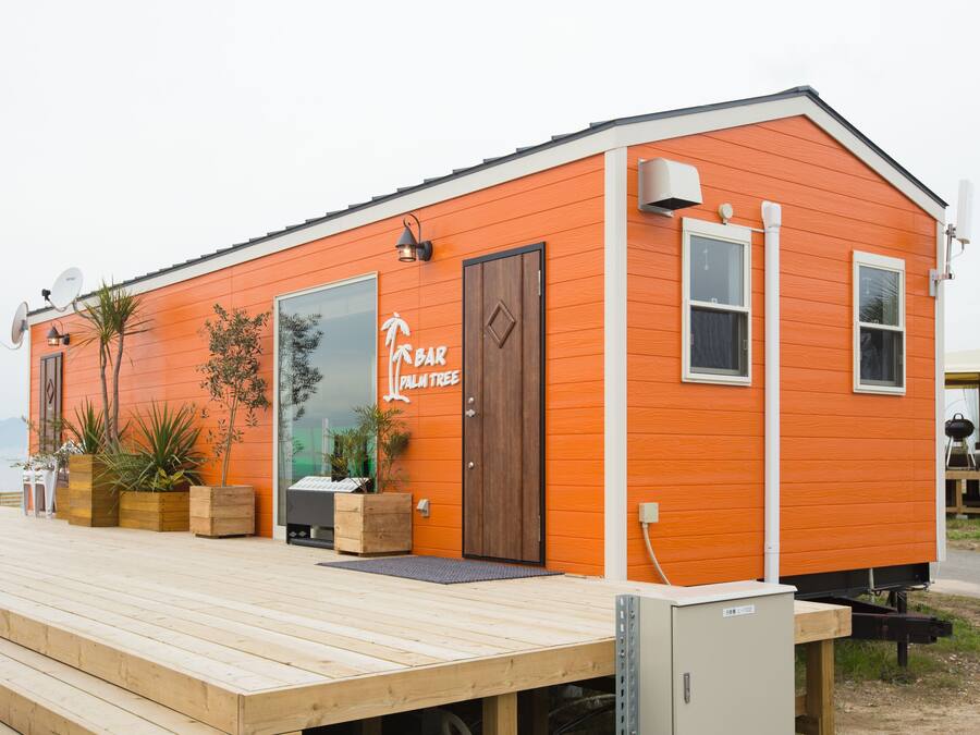 Un pequeño edificio naranja con una terraza de madera, un letrero que dice "Palm Tree Bar" y plantas en macetas.