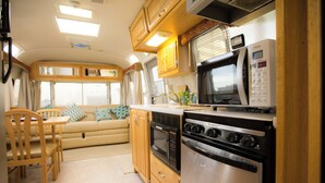 A compact kitchen with a microwave, oven, and refrigerator. There is a wooden dining table with chairs and a sofa in the living area. - Grand Camping Palm Garden Maishima (Osaka)