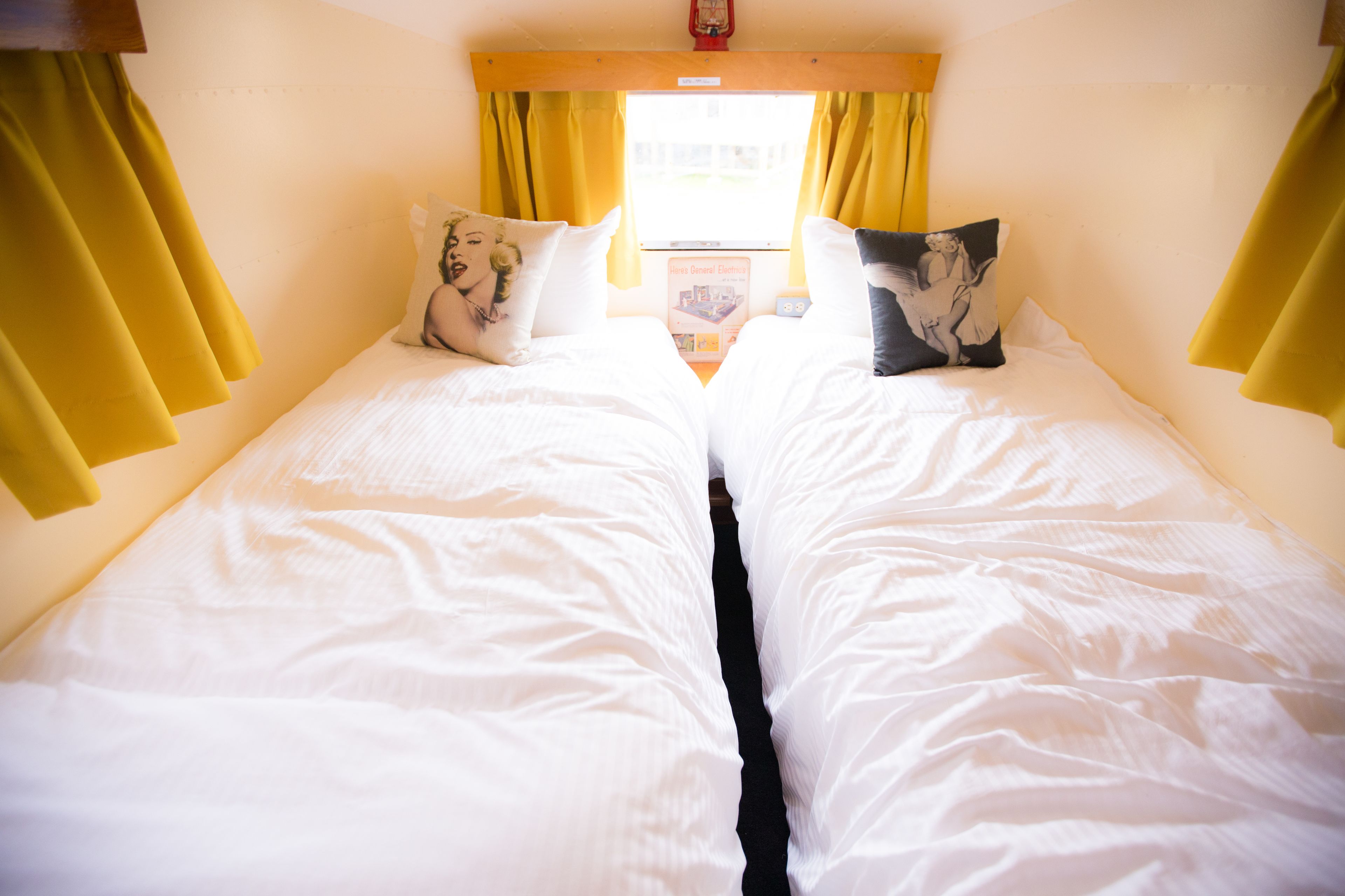 A double bed with white bedding and two pillows, one with a floral design and the other with a black and white image.