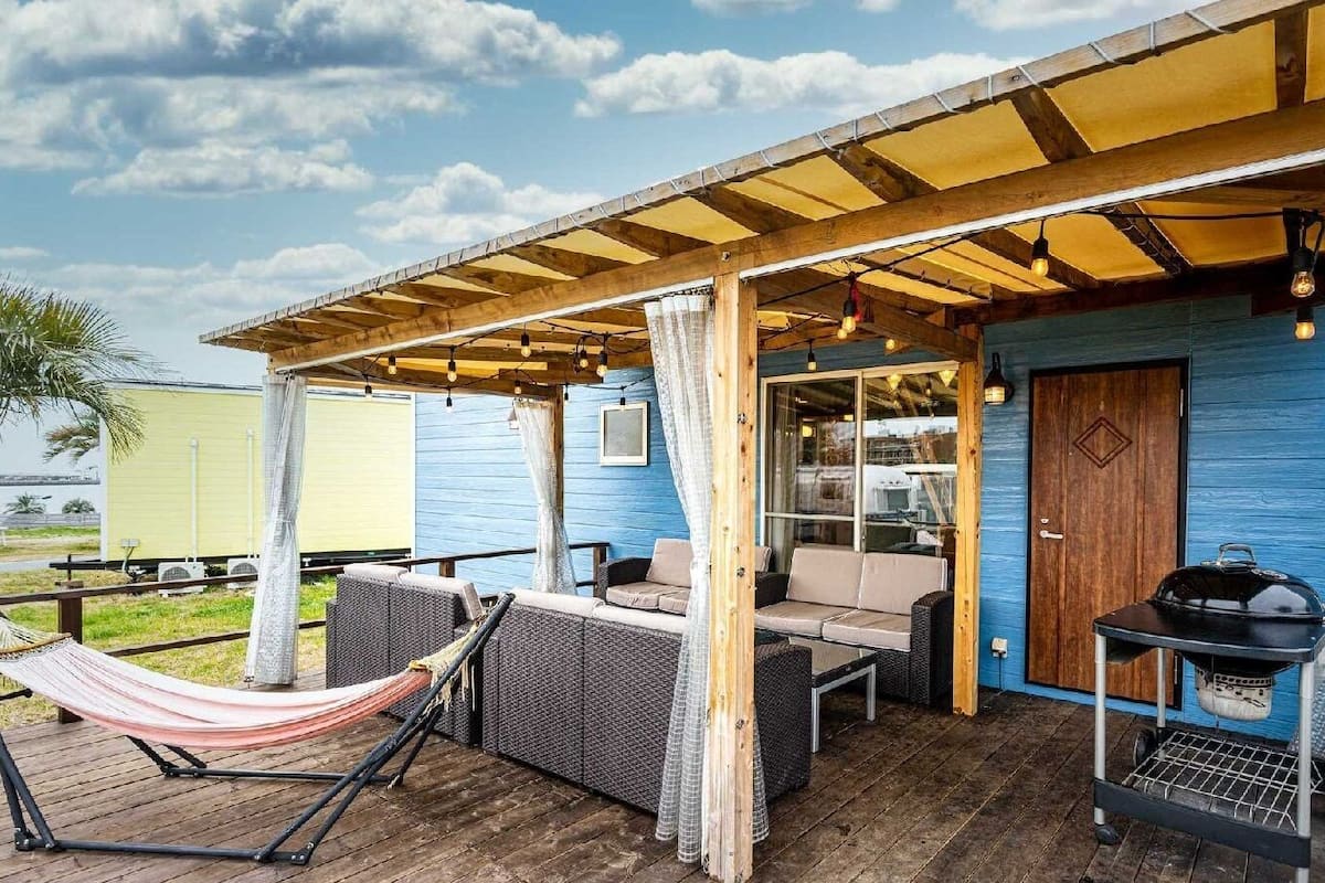 A covered outdoor seating area with wicker furniture, a hammock, and a barbecue grill.