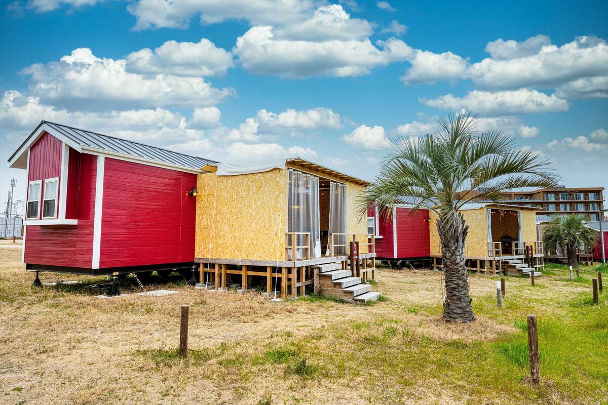 Eine Reihe von Strandhäusern mit Holzterrasse und einer Palme im Vordergrund.