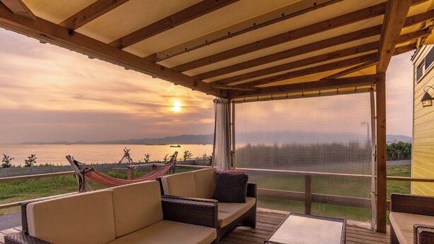 A covered outdoor seating area with a view of the water and mountains. - Grand Camping Palm Garden Maishima (Osaka)