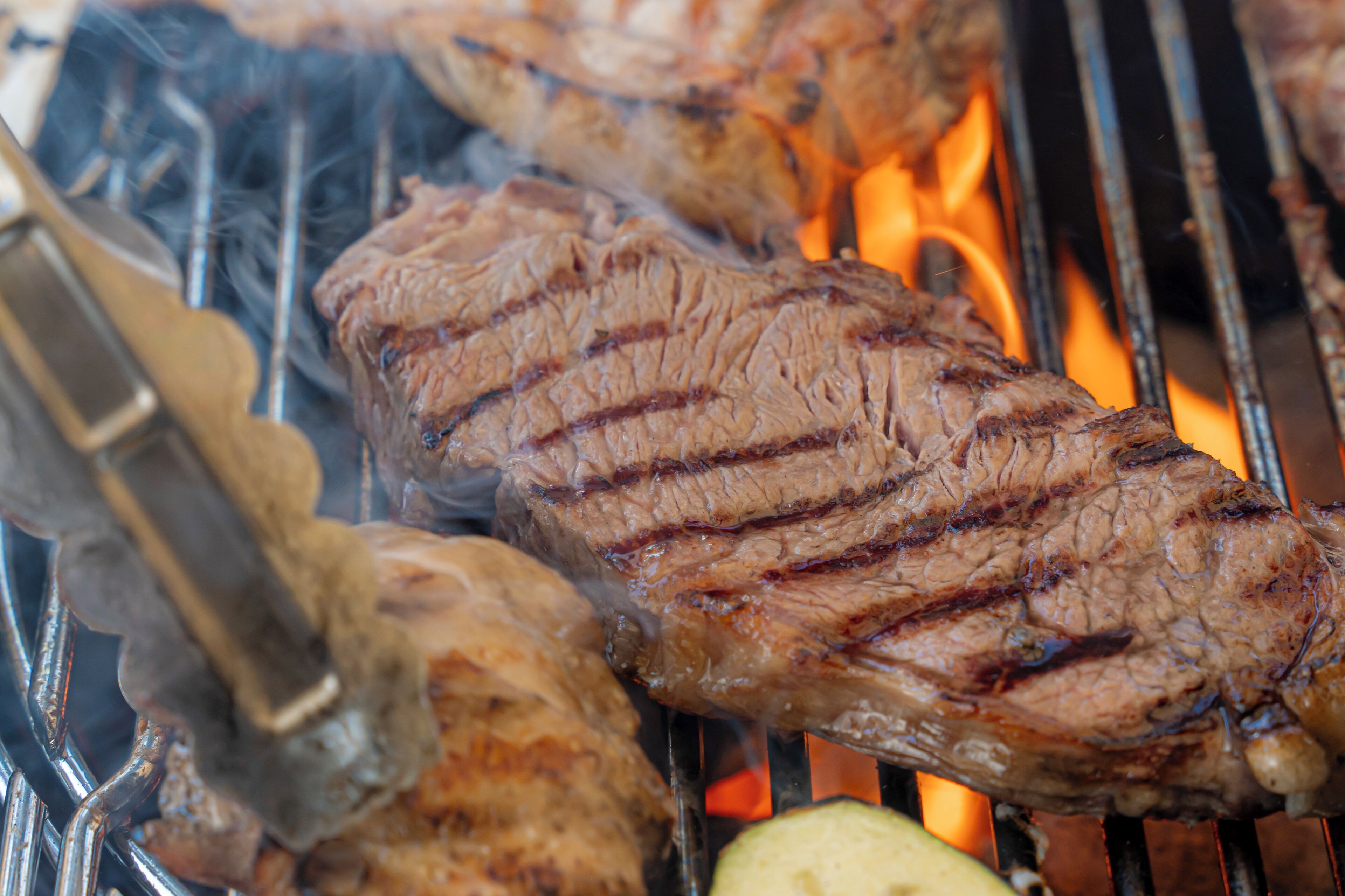 Primer plano de carne a la parrilla con marcas visibles de la parrilla, cocinándose sobre llamas abiertas.
