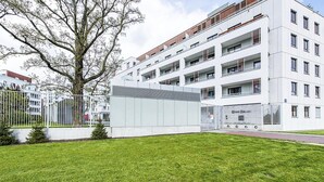 Un edificio moderno con diversi balconi, un grande albero di fronte e un prato curato.