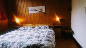 A wooden-paneled room with a bed, two bedside lamps, a framed picture on the wall, and a small stool.